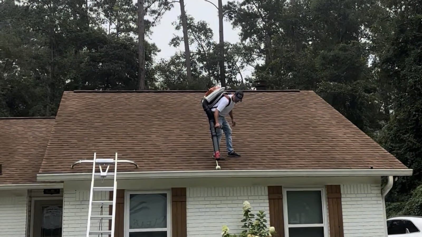 Clear Flow technician working a gutter run from the roof with the ladder set against the eave